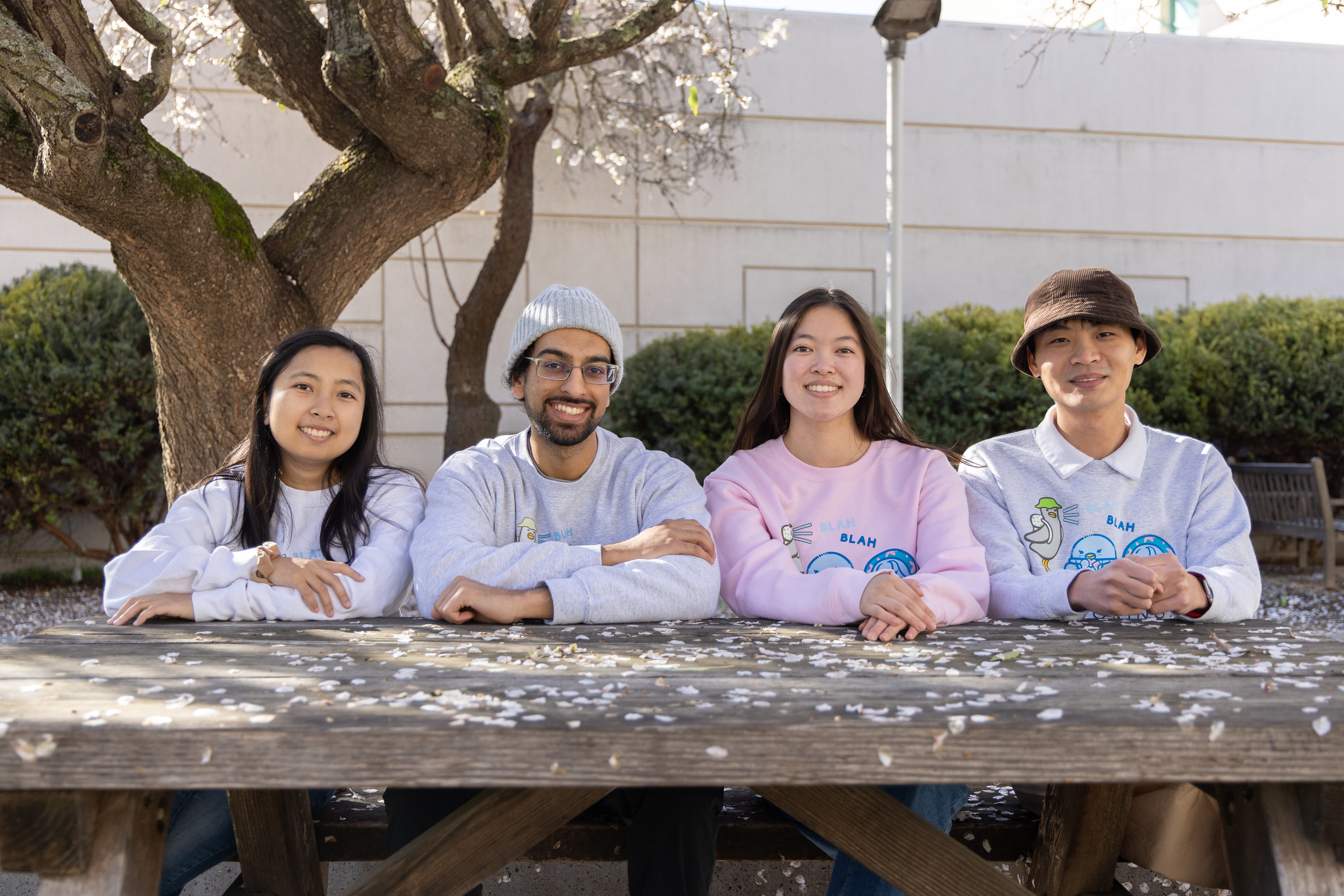 Four people sit a wooden bench outside