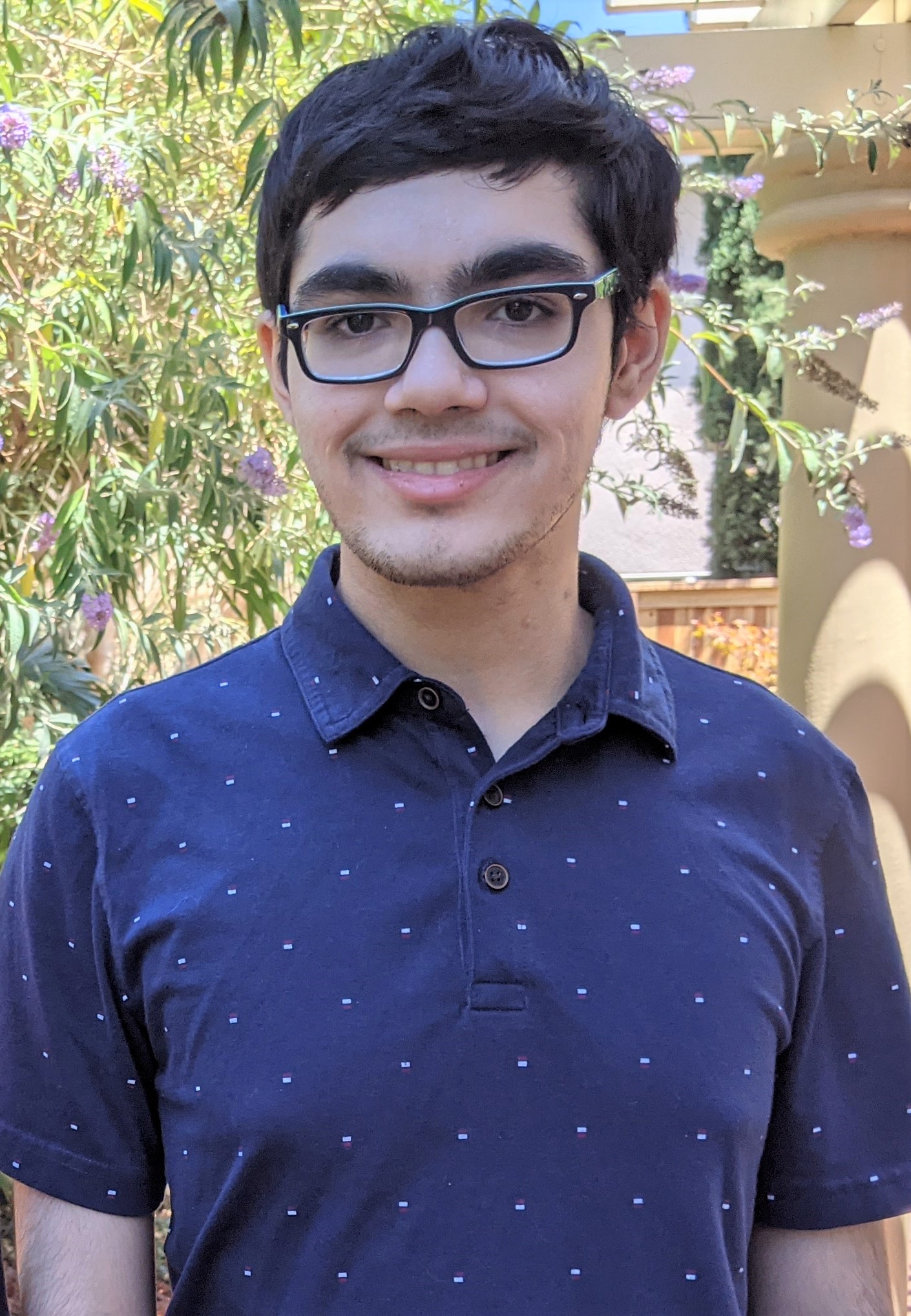 A young light-skinned man with glasses and a dark polo shirt