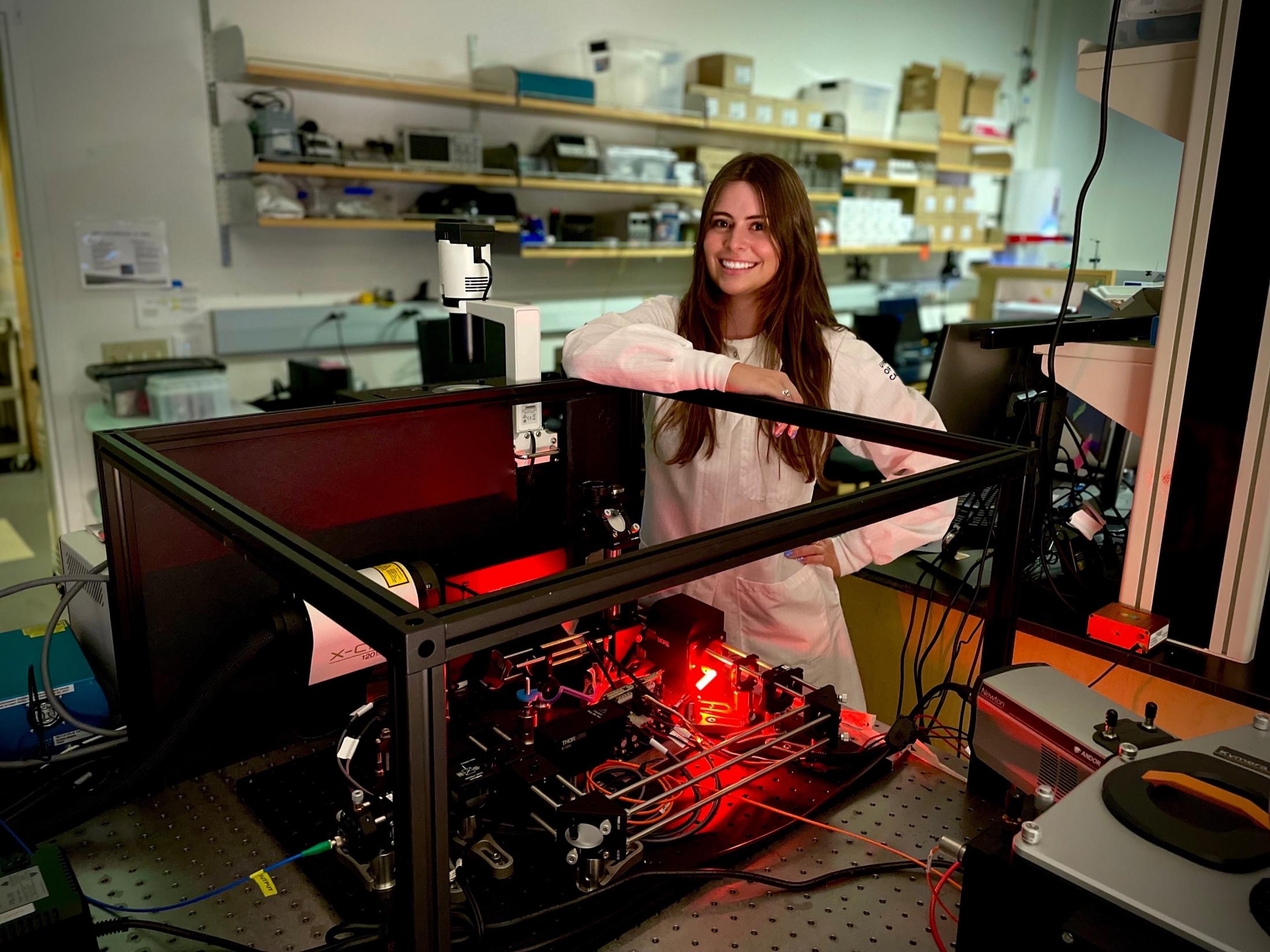 Woman inside a laboratory, at a desk with equipment on shelves behind her