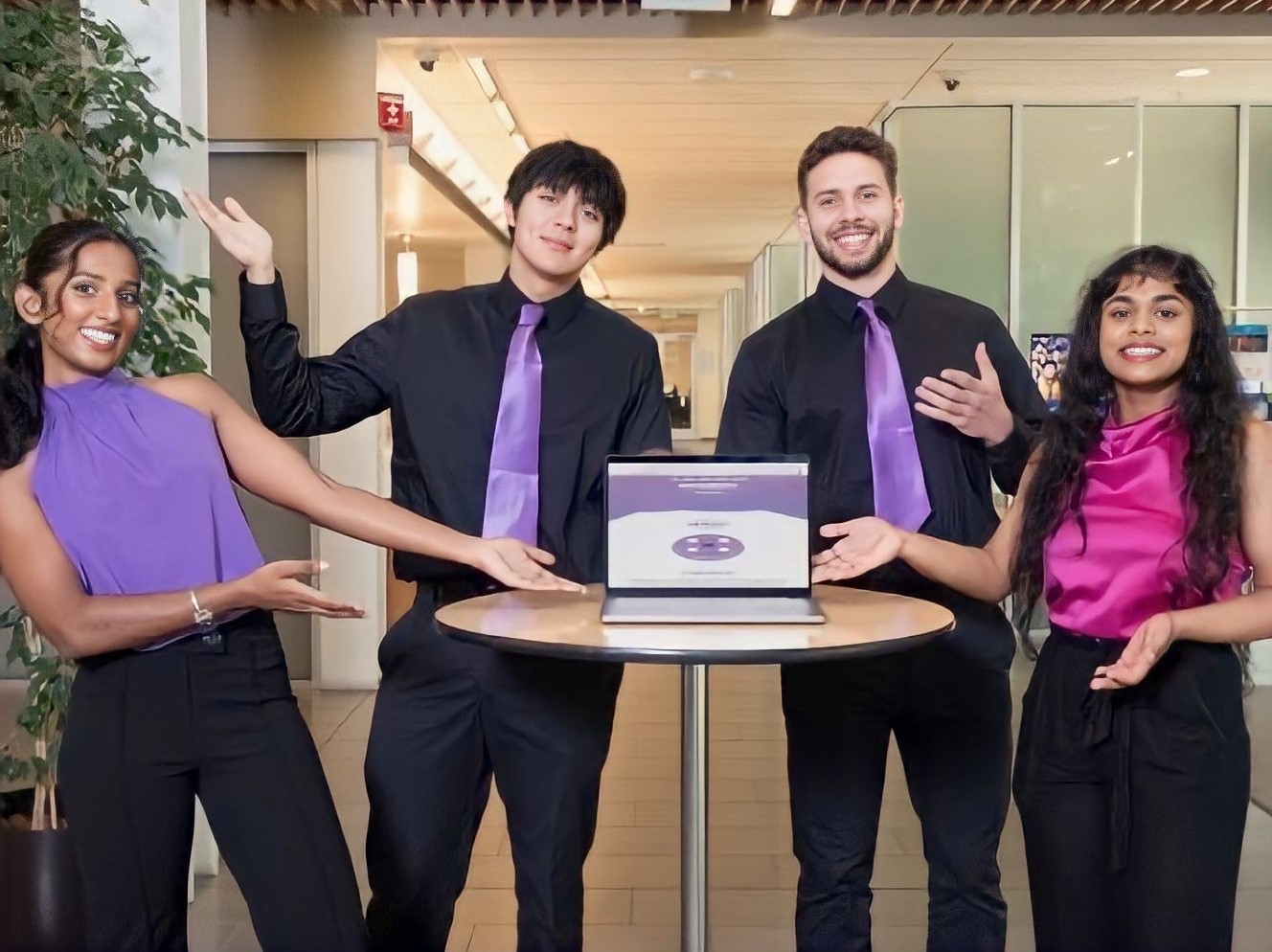 Four UC Davis students from a startup team pose in front of a table with a laptop open to a pitch presentation slide