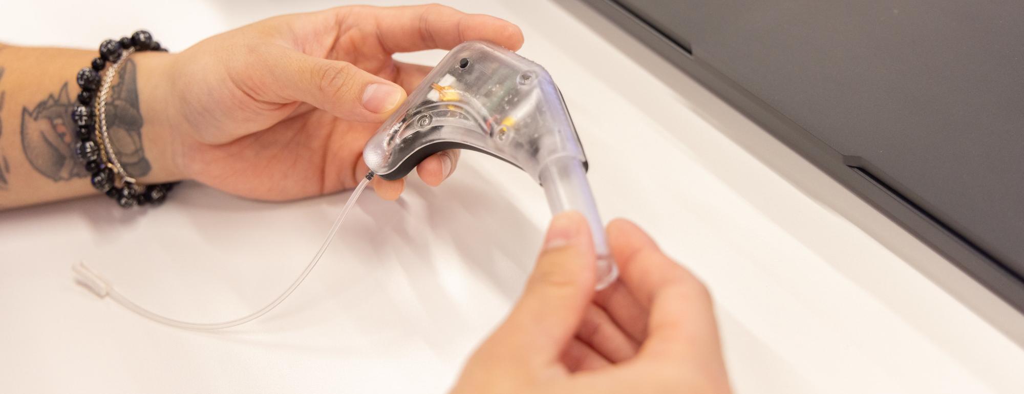 Close-up of hands holding a small clear prototype for a wearable ear device