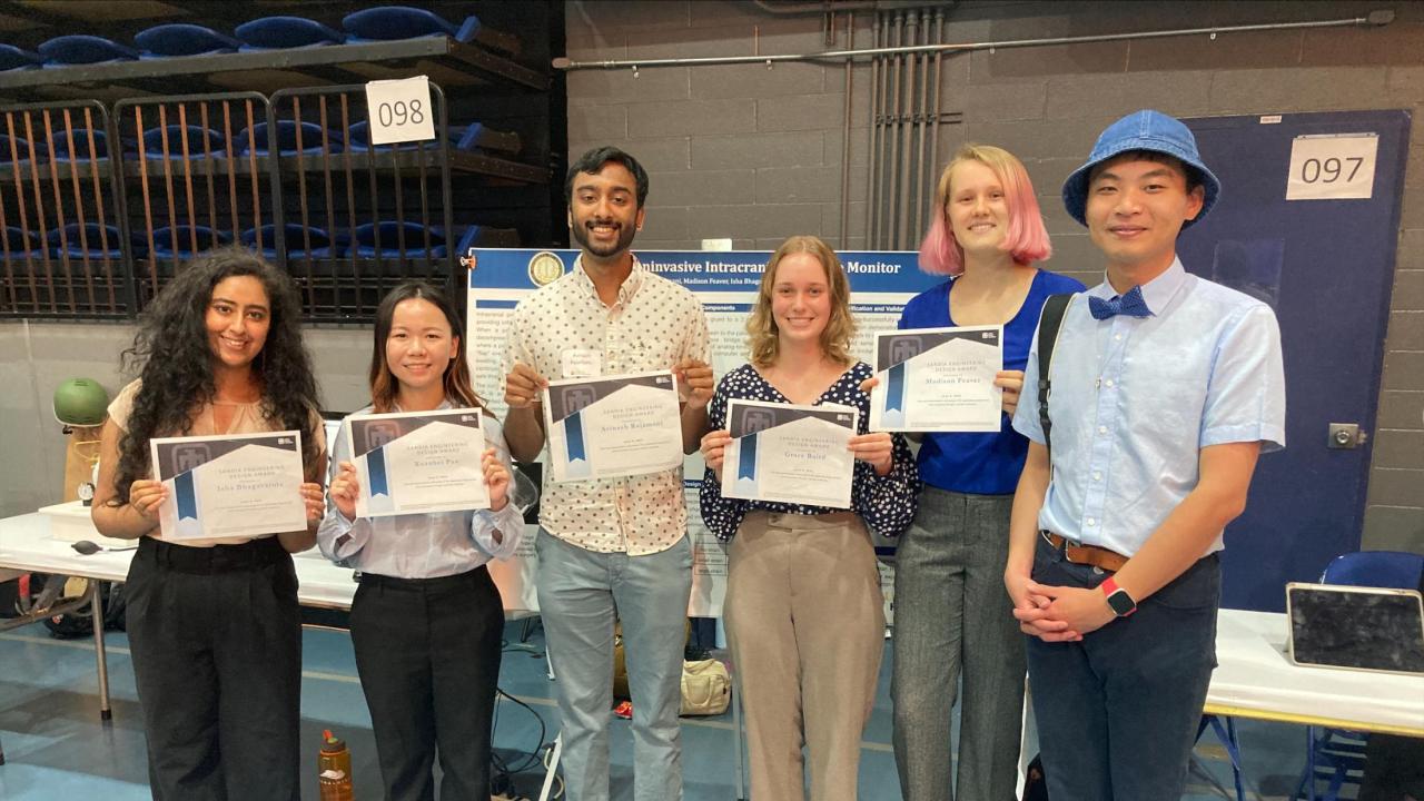 Six people stand for a group photo, five of them hold up certificates