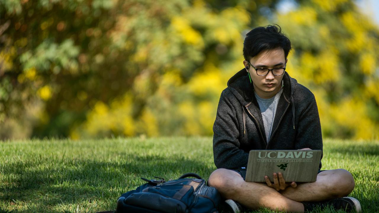 student sitting in grass with laptop