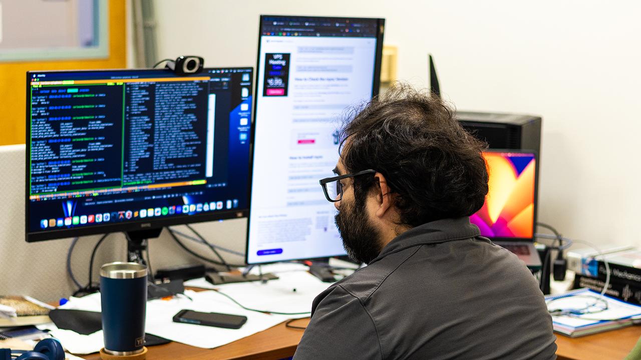 Person sits at a computer with three monitors