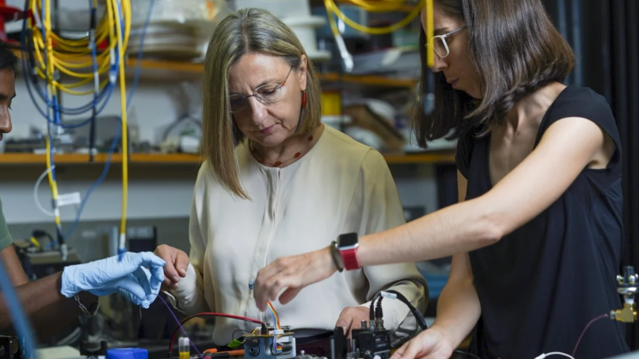Three people in a lab with gloves on touching different color cables