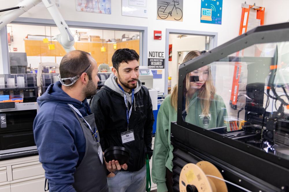 Two men and a woman engage in coversation inside a 3D printing lab