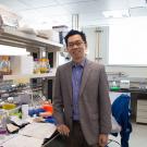 Young Asian man, Dr. Cheemeng Tan, standing in the middle of a laboratory with medical equipment on the benches