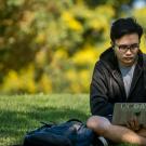 student sitting in grass with laptop