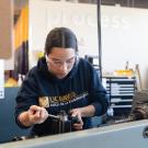 Student with UC Davis College of Engineering sweater works on a machine indoors