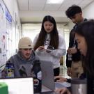 Students gather around a table with laptops in the middle of a hallway
