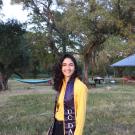 A woman wearing a UC Davis stole smiles in a grassy field 