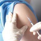 Gloved hands hold syringe up to someone's arm
