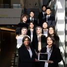 large group of undergraduates in business attire on a staircase with laptop screen showing their startup